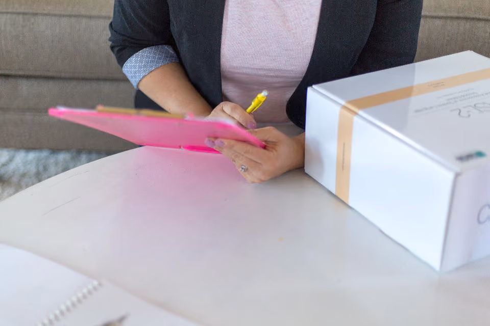 Hand with a pen on a clipboard next to a product box